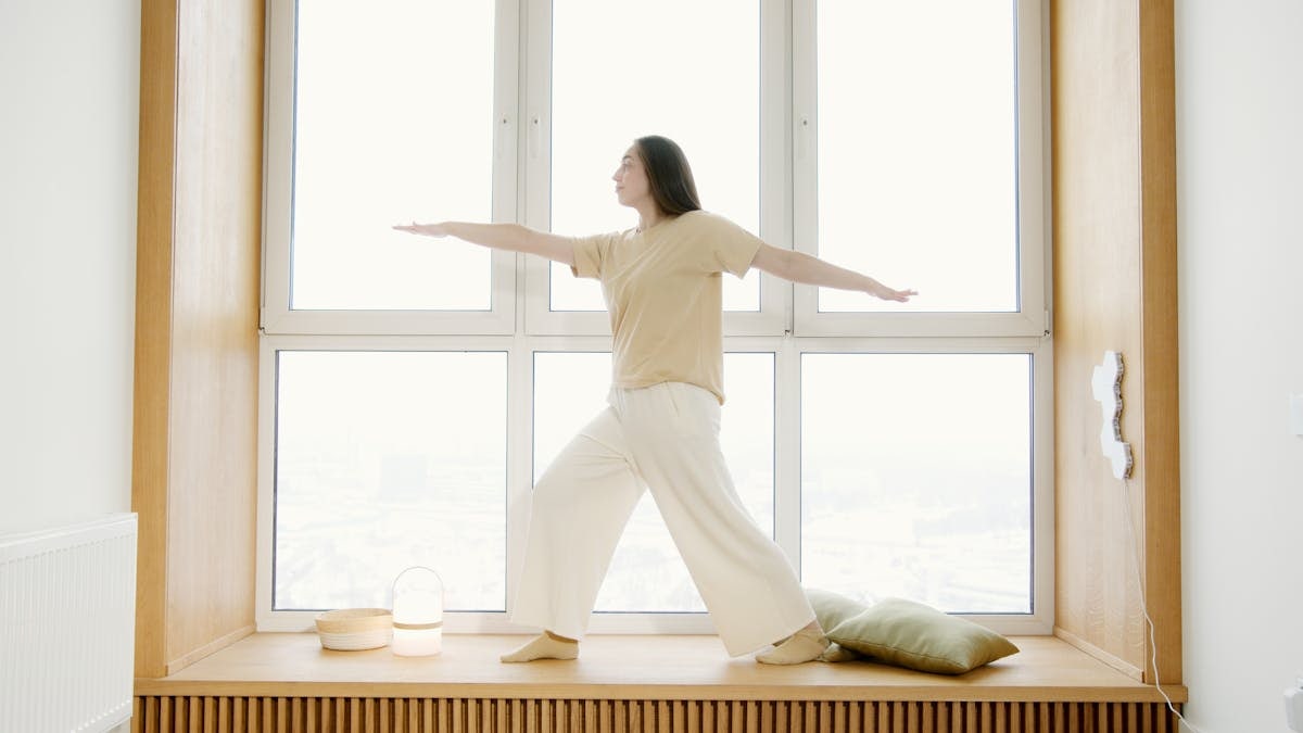A woman balances in a yoga pose on a windowsill with natural light.